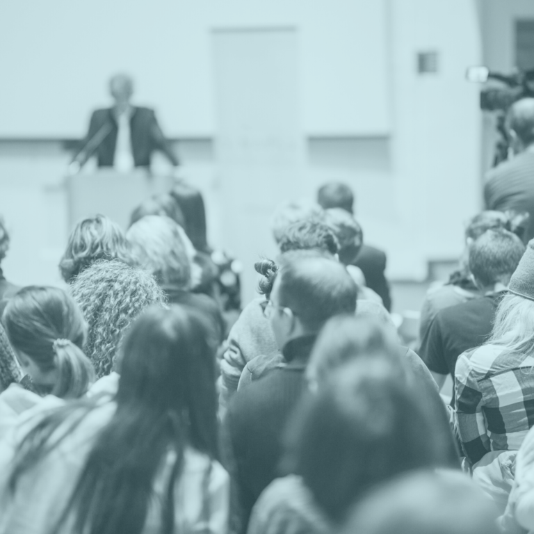 Image of an audience and a speaker at a podium