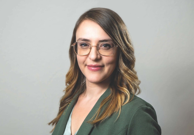 Photo of Dominika Villafuerte-Woszczyk looking into the camera, smiling with hair down, wearing glasses and an Avantpage branded blazer.