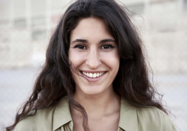 Photo of a woman smiling authentically and looking directly at the camera with an out of focus background