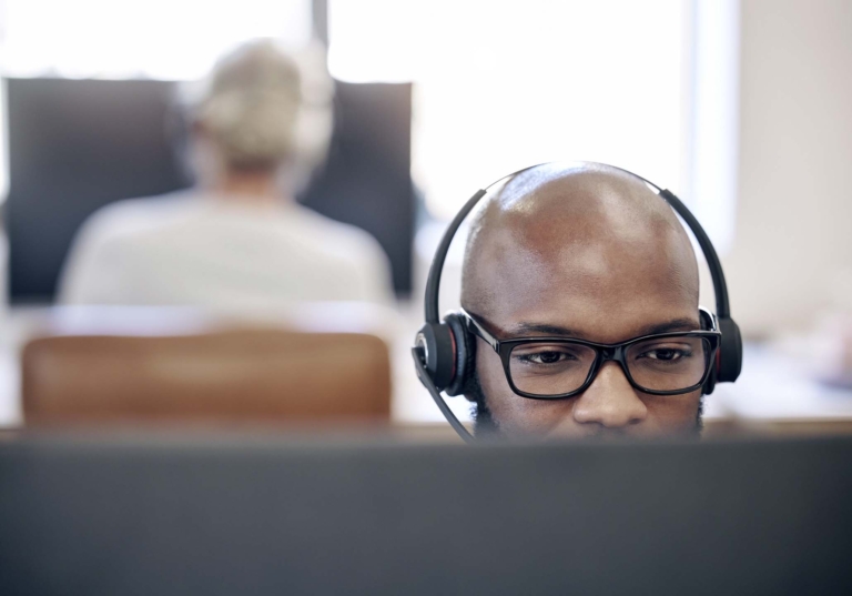 Photo of a man visible from the nose up looking at a computer while he wears headphones