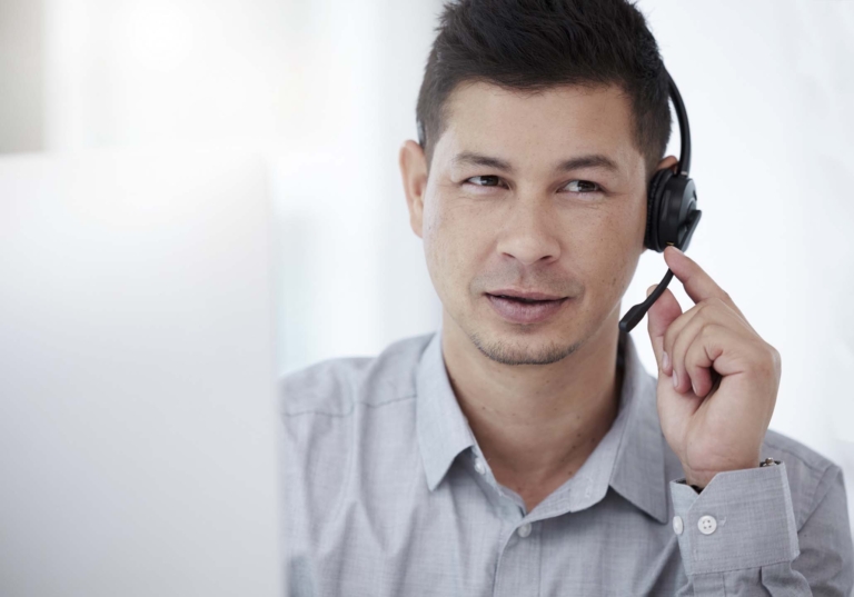 Photo of a man on a headset talking to someone with the corner of a computer in view