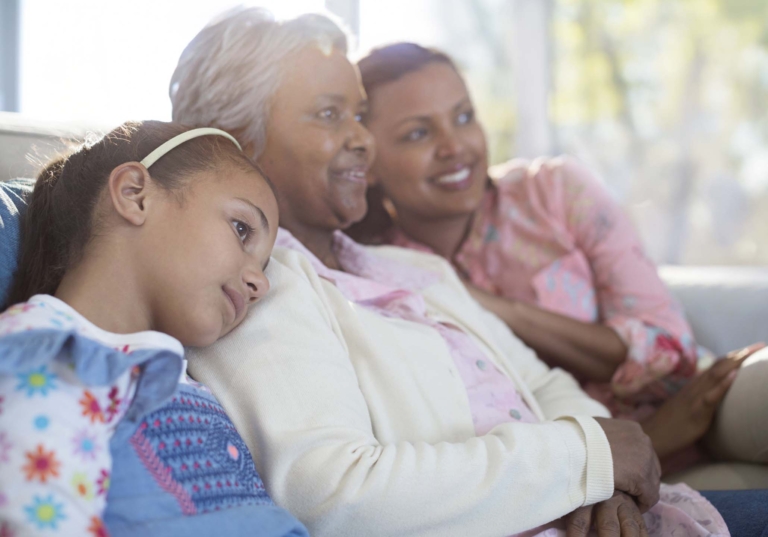 Photo of a family of three women of three generations sitting on a couch together and smiling