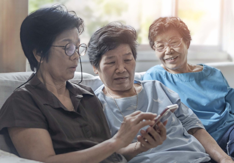 Photo of three women sitting on a couch looking at a cell phone together