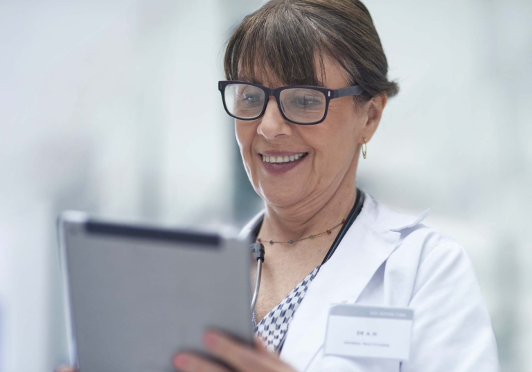 Photo of a doctor who is wearing glasses while looking at a tablet