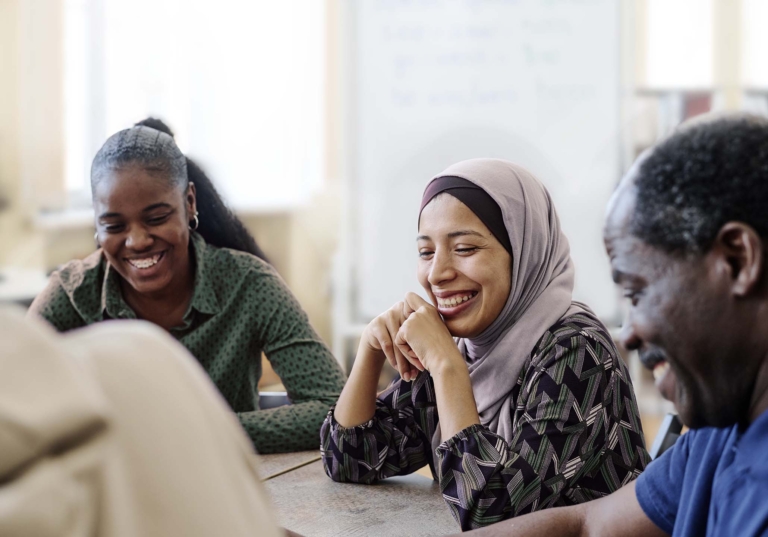 Group of people sitting at a table engaged and laughing with a whiteboard behind them