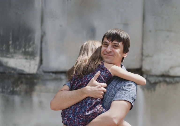 Photo of a man hugging and holding a young girl while smiling to emphasize the quality of life that government translations provide to all individuals.