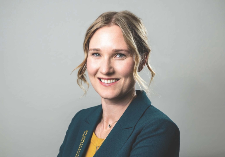 Photo of Nicole Spyt-James looking directly at camera smiling with hair pulled back, and wearing an Avantpage branded blazer