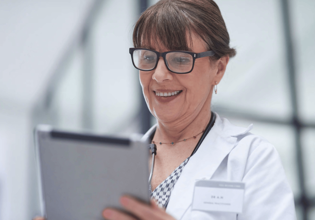 Photo of a doctor who is wearing glasses while looking at a tablet